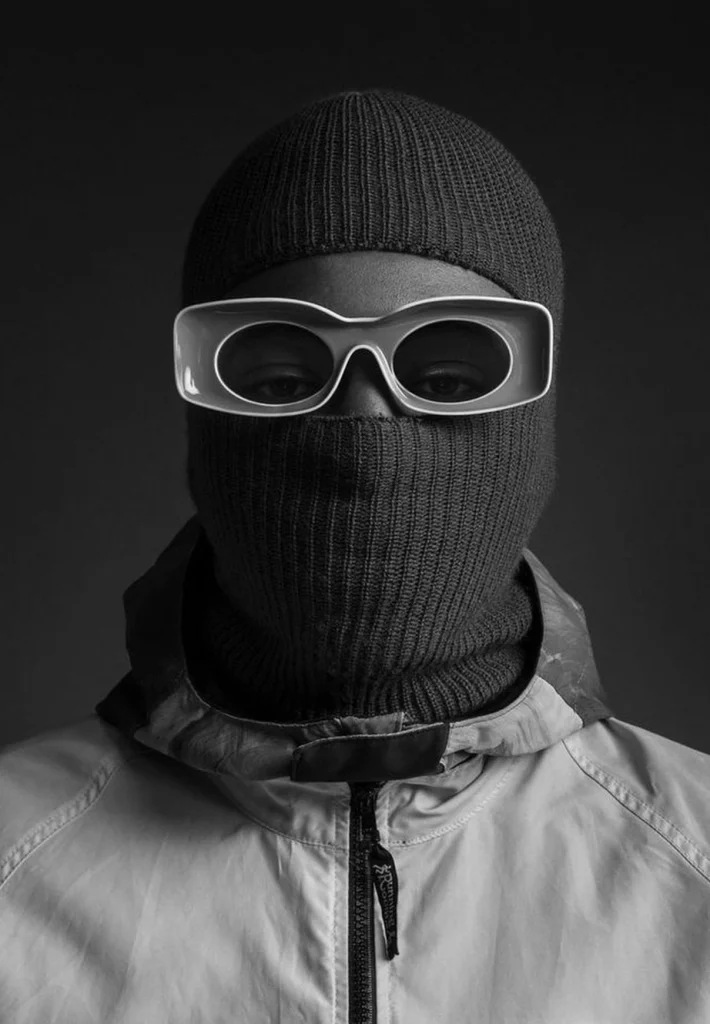 a greyscale image of a Black man in a balaclava and a jacket, wearing ceramic eyewear