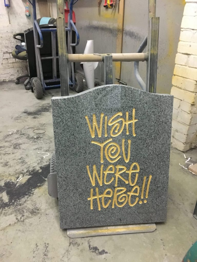 a grey marble tombstone that says "wish you were here!!" in big gold engraved writing